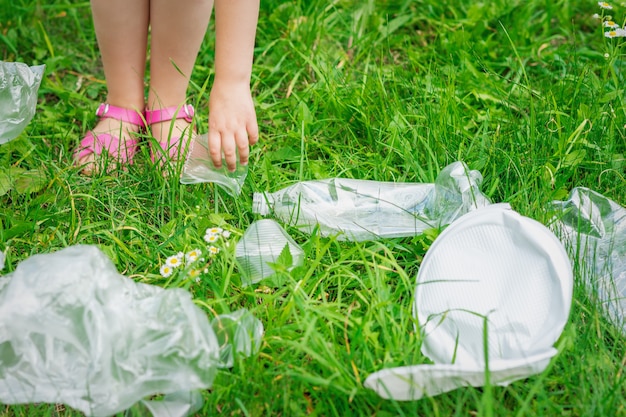 La mano del bambino pulisce l'erba verde dalla spazzatura di plastica