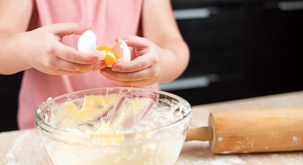 la mano del bambino rompe un uovo in una ciotola di pasta per biscotti