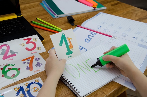 La mano del bambino tiene un pennarello verde e scrive la parola UNO Nelle mani di una carta con il numero