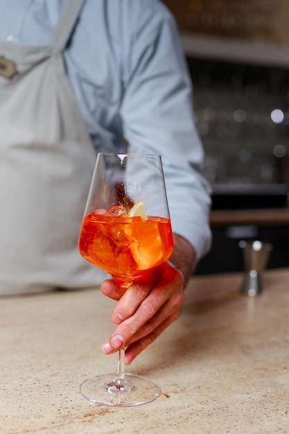 La mano del barista con un bicchiere di cocktail con il primo piano di ghiaccio