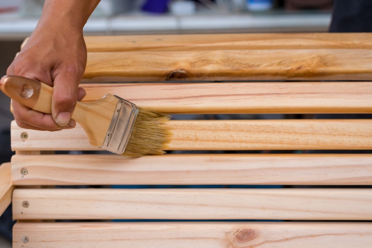 La mano del giovane che tiene una spazzola che applica la pittura della vernice su una mobilia di legno