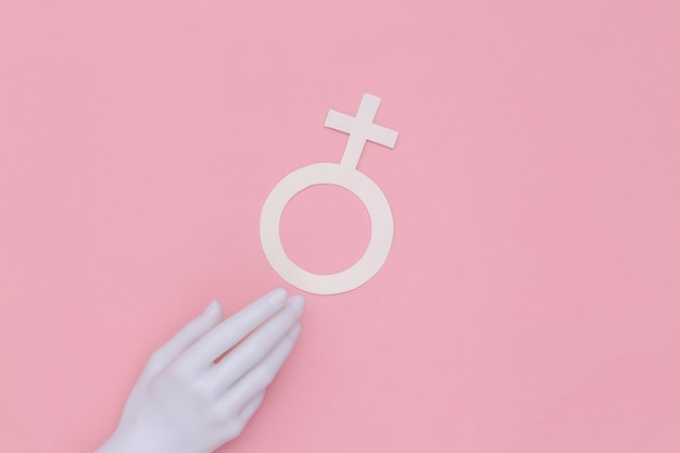 La mano del manichino tocca il simbolo del genere femminile su uno sfondo rosa. Vista dall'alto