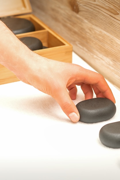 La mano del massaggiatore espone le pietre di massaggio sul tavolo nel salone della stazione termale