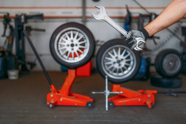 La mano del meccanico automatico tiene la chiave, servizio pneumatici. Ispezione professionale di pneumatici per automobili in officina, ruote su martinetti di sollevamento, riparazione di strumenti e attrezzature