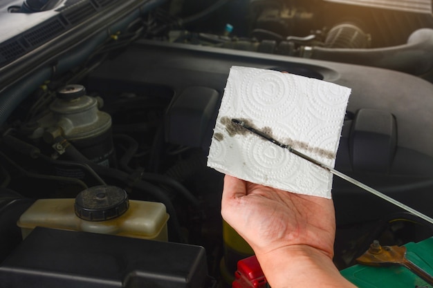 La mano del meccanico controlla il livello e il colore dell'olio motore nel motore di un'auto durante la manutenzione