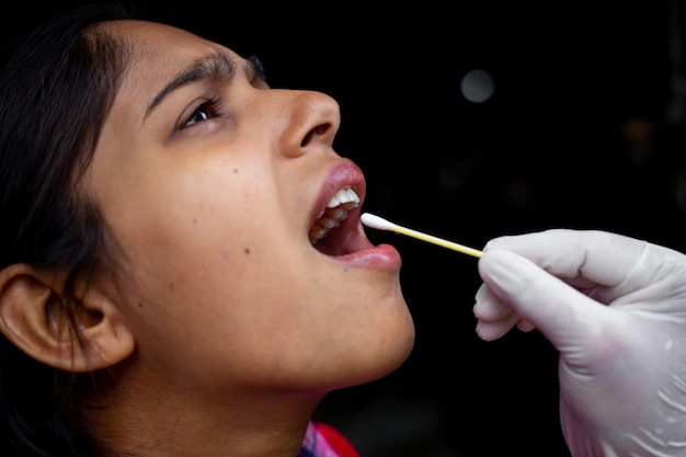 La mano del medico che prende il test della saliva dalla bocca di una giovane donna con tampone di cotone Raccolta di campioni di coronavirus della gola Viste del primo piano