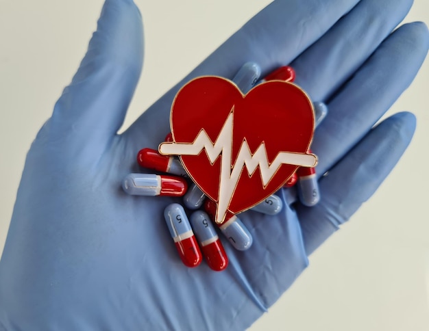 La mano del medico nel guanto tiene il simbolo del cuore rosso e le pillole del cuore