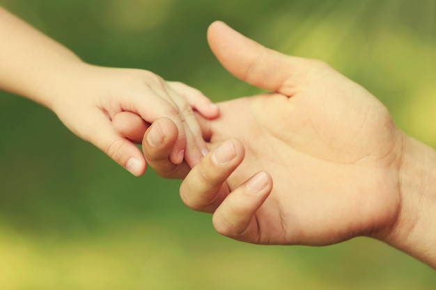 La mano del padre conduce sua figlia all'aperto su sfondo verde sfocato fiducia nel concetto di famiglia