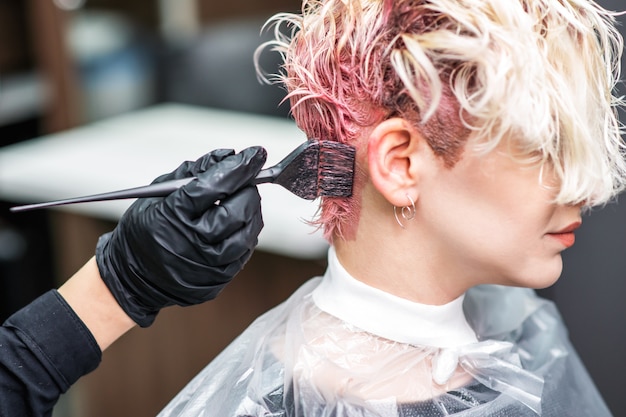 La mano del parrucchiere in guanti neri dipinge i capelli della donna in un colore rosa.