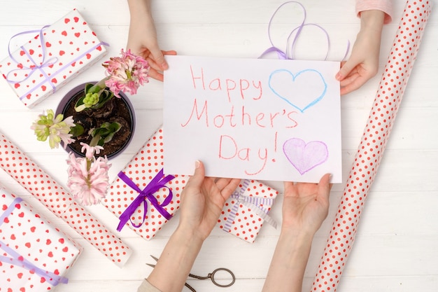 La mano del piccolo bambino che dà una cartolina dipinta a mano alla mano di sua madre, vista dall'alto. Regali per la felice festa della mamma