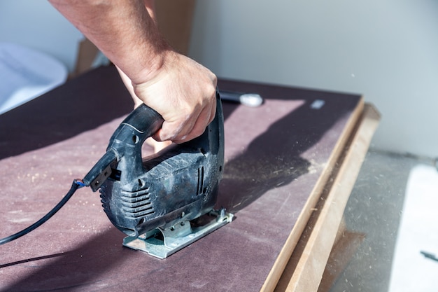 La mano del primo piano dell'operaio con l'utensile da taglio professionale, ha tagliato il ripiano del tavolo di legno