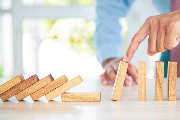 La mano del primo piano impedisce al blocco di legno di non cadere concetti di domino di gestione del rischio finanziario e pianificazione strategica e piano di sfida aziendale