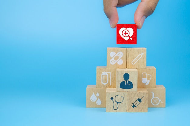 La mano del primo piano sceglie i blocchi di legno di un giocattolo del cubo con un'icona del cuore impilata in una forma della piramide per i concetti medici e dell'assicurazione malattia.