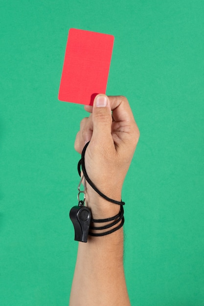 La mano dell'arbitro che tiene un cartellino rosso e un fischio su sfondo verde.