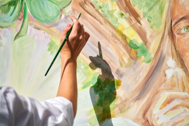 La mano dell'artista della ragazza tiene il pennello e disegna il paesaggio verde della natura su tela