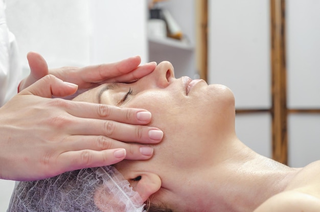 La mano dell'estetista applica la crema sul viso della donna nel salone spa Viso rilassato sul divano Pelle ringiovanente