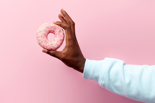 la mano dell'uomo afroamericano tiene una dolce ciambella rotonda su sfondo rosa isolato