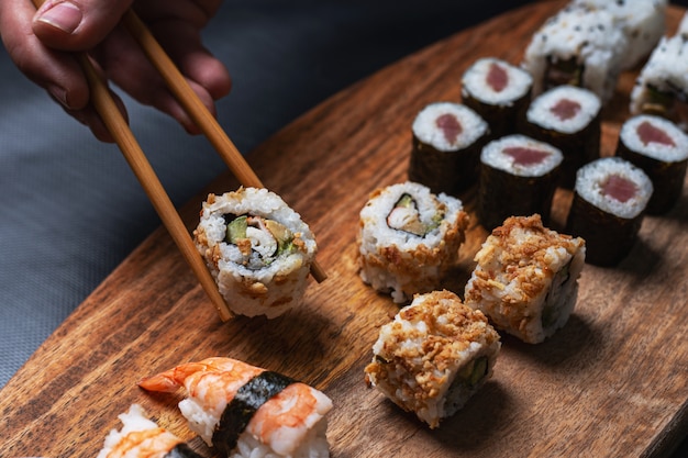 la mano dell'uomo cattura sushi da tavola di legno con composizione di più pezzi. Cucina gastronomica giapponese.