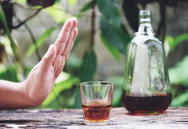 La mano dell'uomo che rifiuta il vetro con la bevanda alcolica sulla superficie della tavola all'aperto rifiuta di bere un whisky dell'alcool