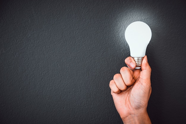 La mano dell&#39;uomo che tiene la lampadina del LED sopra la parete nera