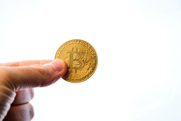 La mano dell'uomo che tiene una moneta bitcoin con due dita su uno sfondo bianco