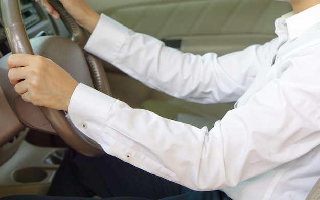 La mano dell'uomo indossa una camicia bianca che tiene il volante mentre guida un'auto