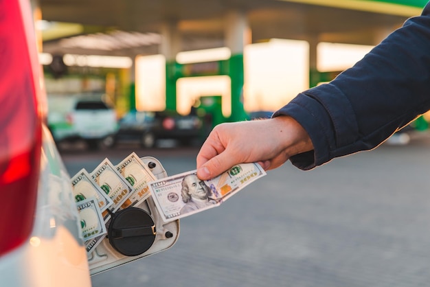 La mano dell'uomo mette i soldi nel serbatoio dell'auto. rifornimento auto. concetto di stazione di servizio