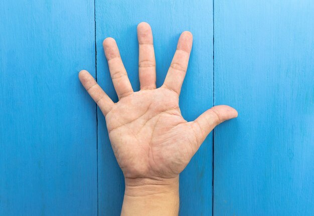 La mano dell&#39;uomo si è alzata contro su fondo di legno blu