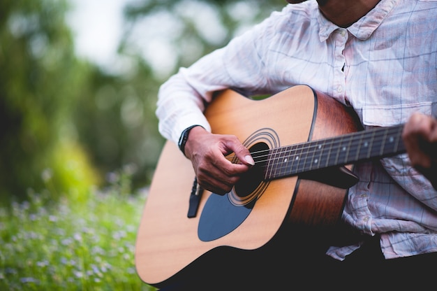 La mano dell&#39;uomo suona la chitarra acustica, suona la chitarra solo in giardino