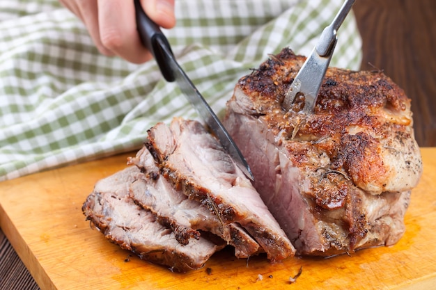 La mano dell'uomo taglia la carne al forno con un coltello sul tagliere