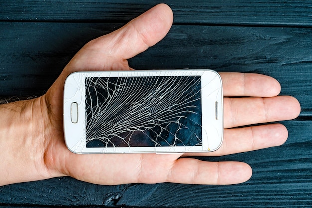 La mano dell'uomo tiene il telefono cellulare con touchscreen rotto su sfondo scuro Smartphone con schermo rotto rotto nel palmo dell'uomo