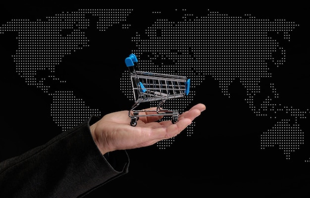 La mano dell'uomo tiene un carrello della spesa in miniatura su uno sfondo scuro concetto dell'inizio delle vendite mondiali la crescita degli acquisti Acquisti online