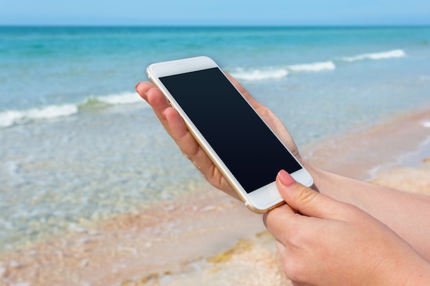 La mano della bella donna facendo uso dello Smart Phone alla spiaggia