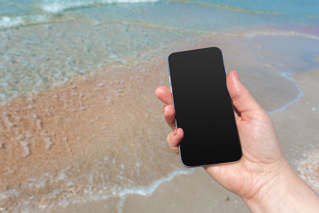 La mano della bella donna facendo uso dello Smart Phone alla spiaggia