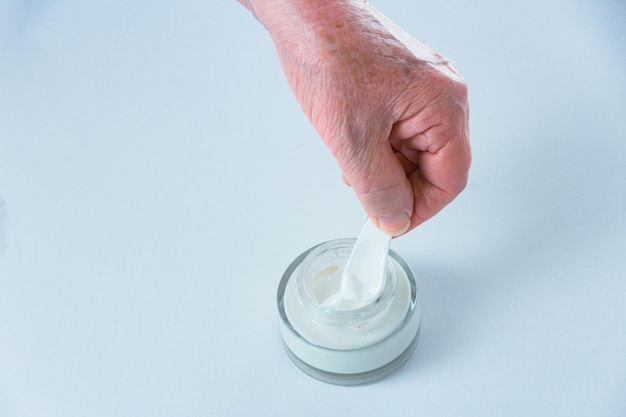 La mano della donna anziana che prende il prodotto cosmetico dalla pubblicità del barattolo della crema per le mani per i pensionati a st