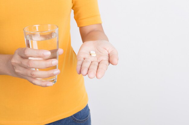 La mano della donna asiatica che tiene gli antidolorifici e il vetro su fondo bianco