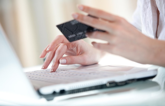 La mano della donna che inserisce i dati utilizzando il laptop mentre si tiene una carta di credito nell'altra mano