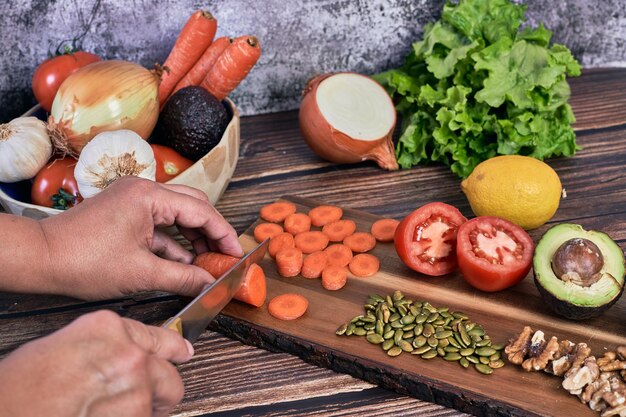 La mano della donna che taglia la carota e altre verdure per fare un'insalata su fondo di legno d'epoca. Cibo vegetariano sano.