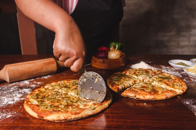 La mano della donna che taglia le pizze a pezzi su un tavolo di legno.