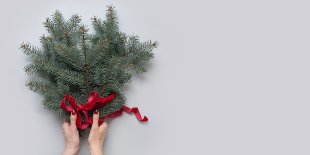 La mano della donna che tiene l'albero di Natale si ramifica con il nastro rosso su gray