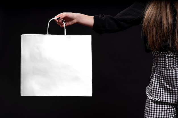 La mano della donna che tiene la borsa bianca su sfondo nero, concetto di shopping. Copia spazio