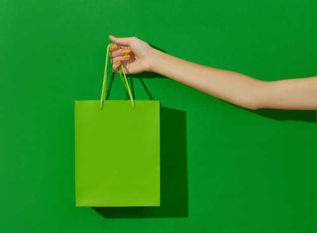 La mano della donna che tiene la borsa della spesa su sfondo verde