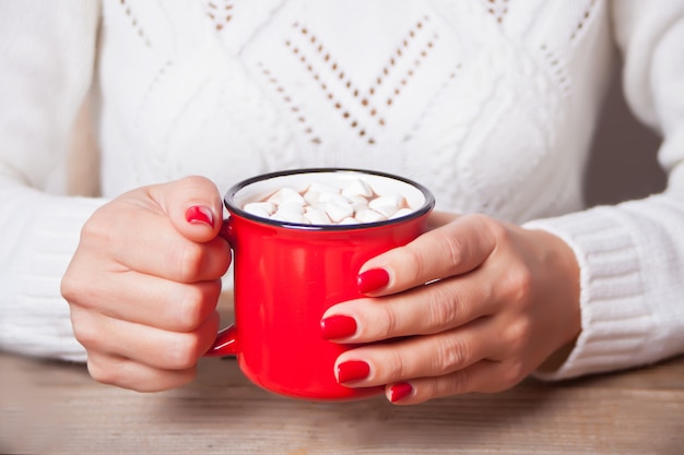 La mano della donna che tiene la tazza rossa di cacao di Natale con caramelle gommosa e molle.