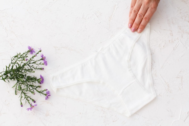 La mano della donna che tiene una bellissima mutandina di cotone bianco sulla superficie strutturata bianca