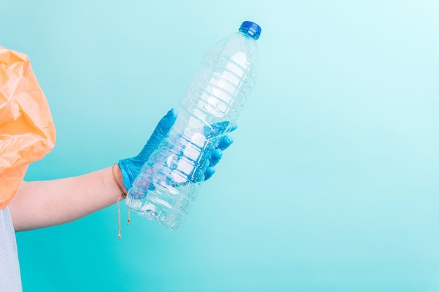 La mano della donna che tiene una bottiglia di plastica per il riciclaggio su sfondo blu. concetto di riciclaggio