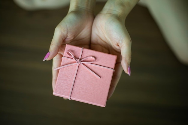 La mano della donna che tiene una scatola regalo rosa dà e ama il concetto