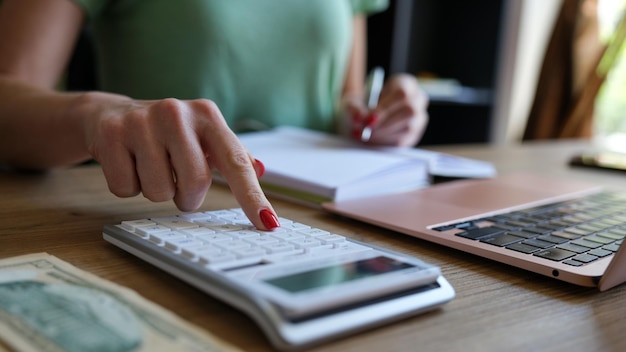 La mano della donna che utilizza una calcolatrice e una lettera prende nota con il calcolo dei costi nell'ufficio a casa