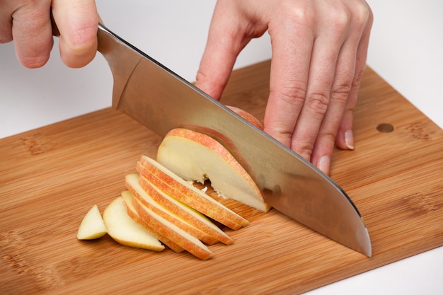 La mano della donna con un coltello da cucina macina la grande mela rossa su un bordo di legno