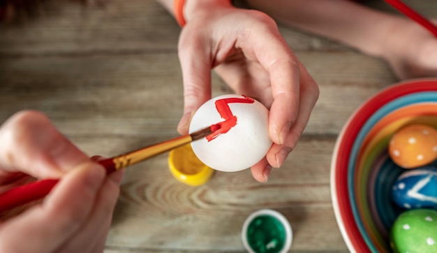 La mano della donna con un pennello sta disegnando un motivo colorato su un uovo di Pasqua Preparazione creativa per le luminose vacanze di Pasqua