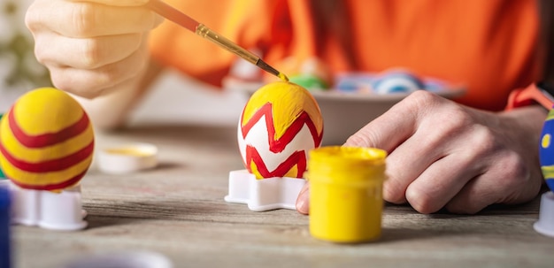 La mano della donna con un pennello sta disegnando un motivo colorato su un uovo di Pasqua Preparazione per le luminose vacanze di Pasqua